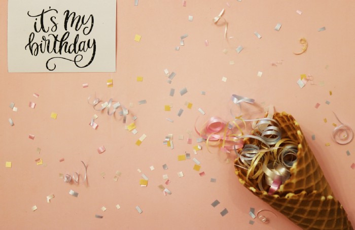 Unsplash stock image of a peach background littered with confetti, a piece of paper with the words “it’s my birthday” and a waffle cone filled with curled ribbon.